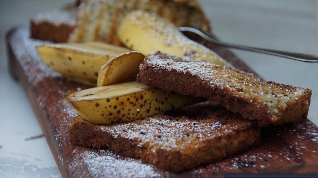 Bolo de banana já assado. Sobre ele fatias de banadas cortadas no comprimento cobertas com açúcar e canela.
