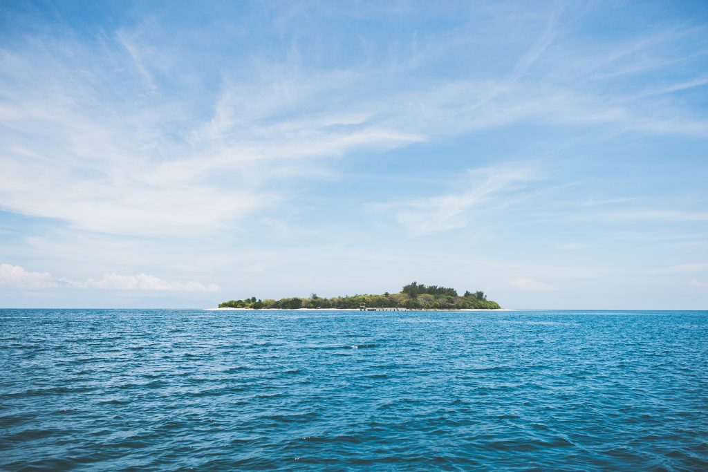 Imagem de uma praia bem azul. Ao fundo uma ilha extensa.
