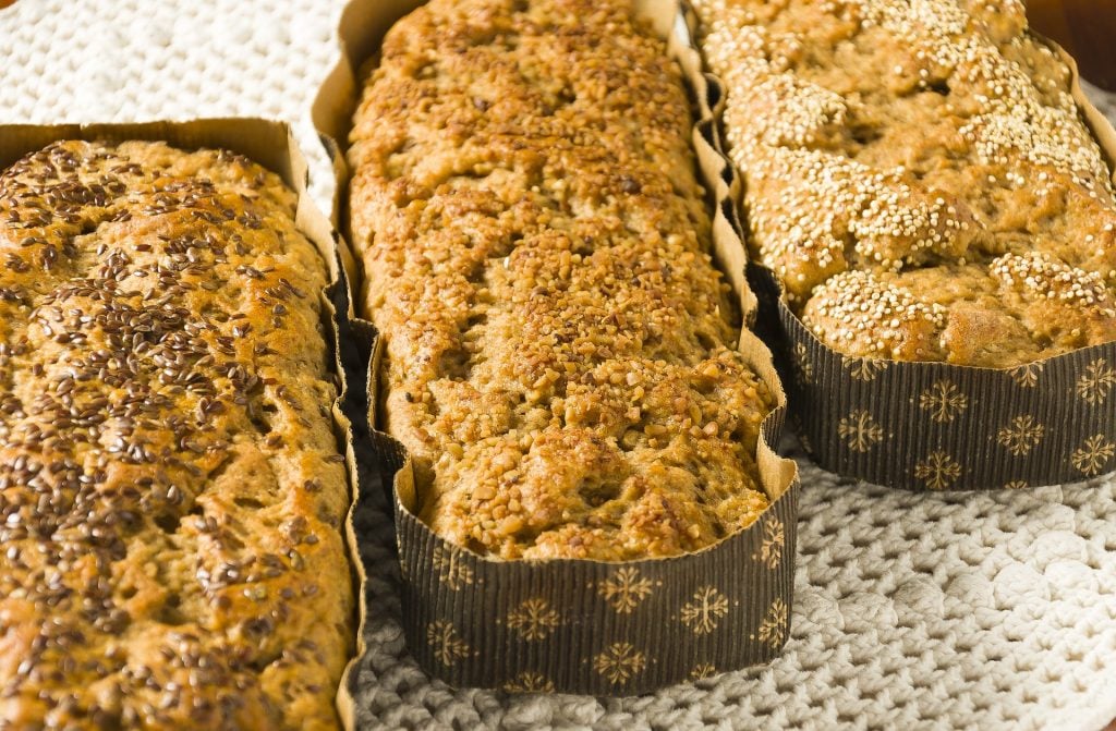 Três formas retangulares de papelão contendo cada uma delas um pão integral de sabor diferenciado.