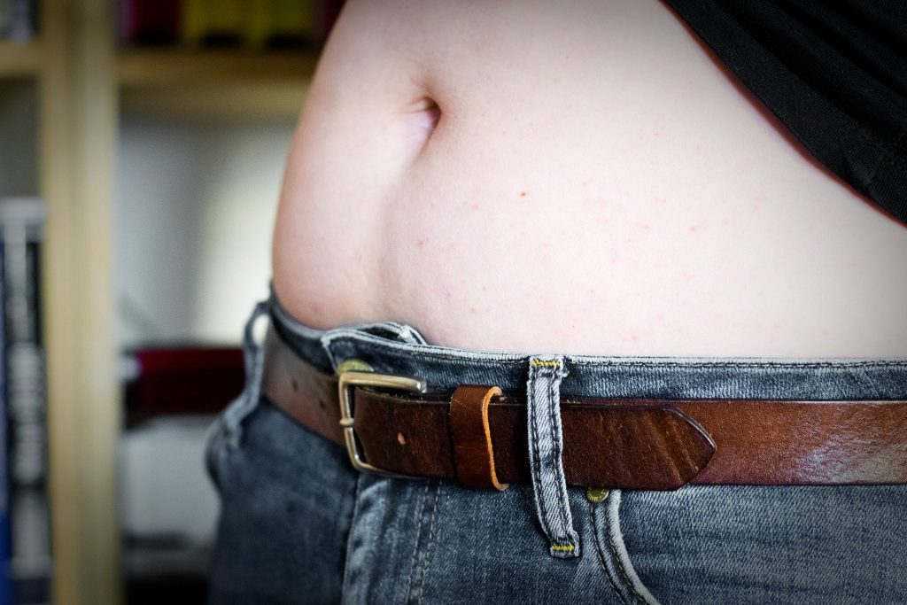 Imagem de uma barriga de uma mulher. Ela veste calça jeans e segura a sua blusa preta, para mostrar a sua barriga.