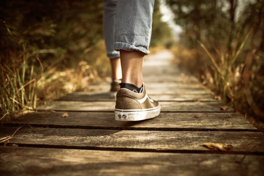 Pessoa usando tênis andando em caminho de madeira no meio de uma floresta.