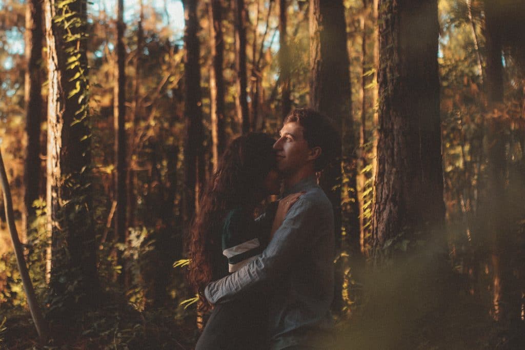 Casal abraçado em floresta com sol entre as árvores