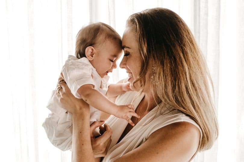 Mãe segurando bebê em frente seu rosto sorrindo