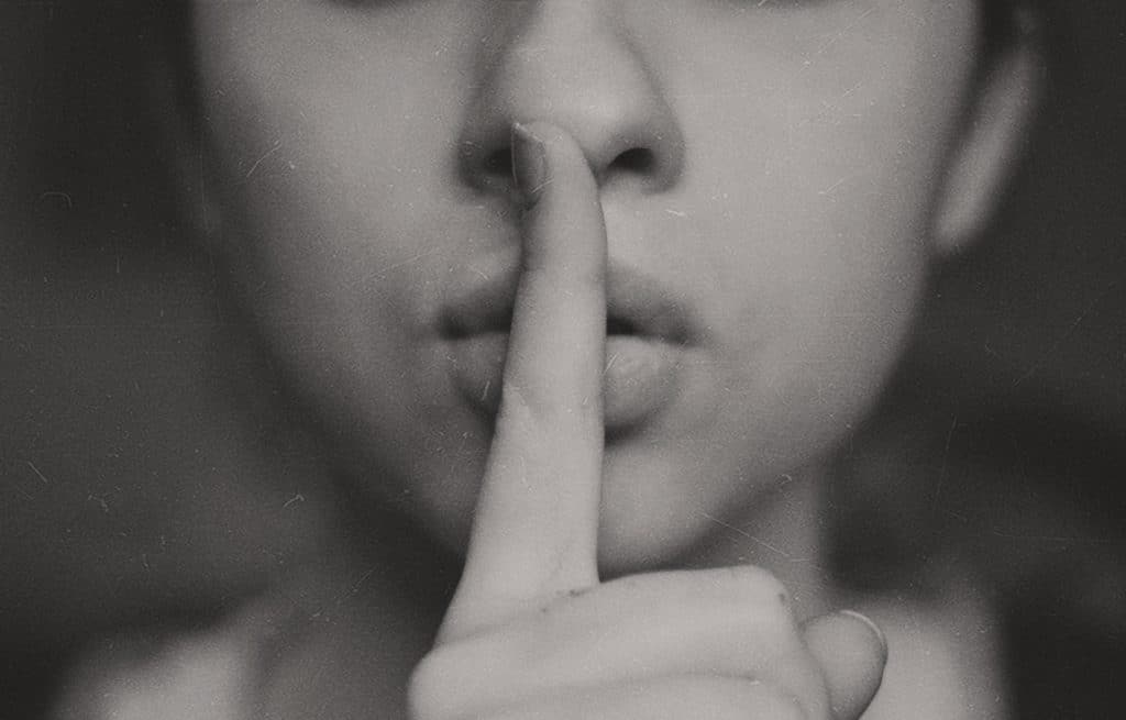 Mulher com o dedo indicador na boca em sinal de silêncio