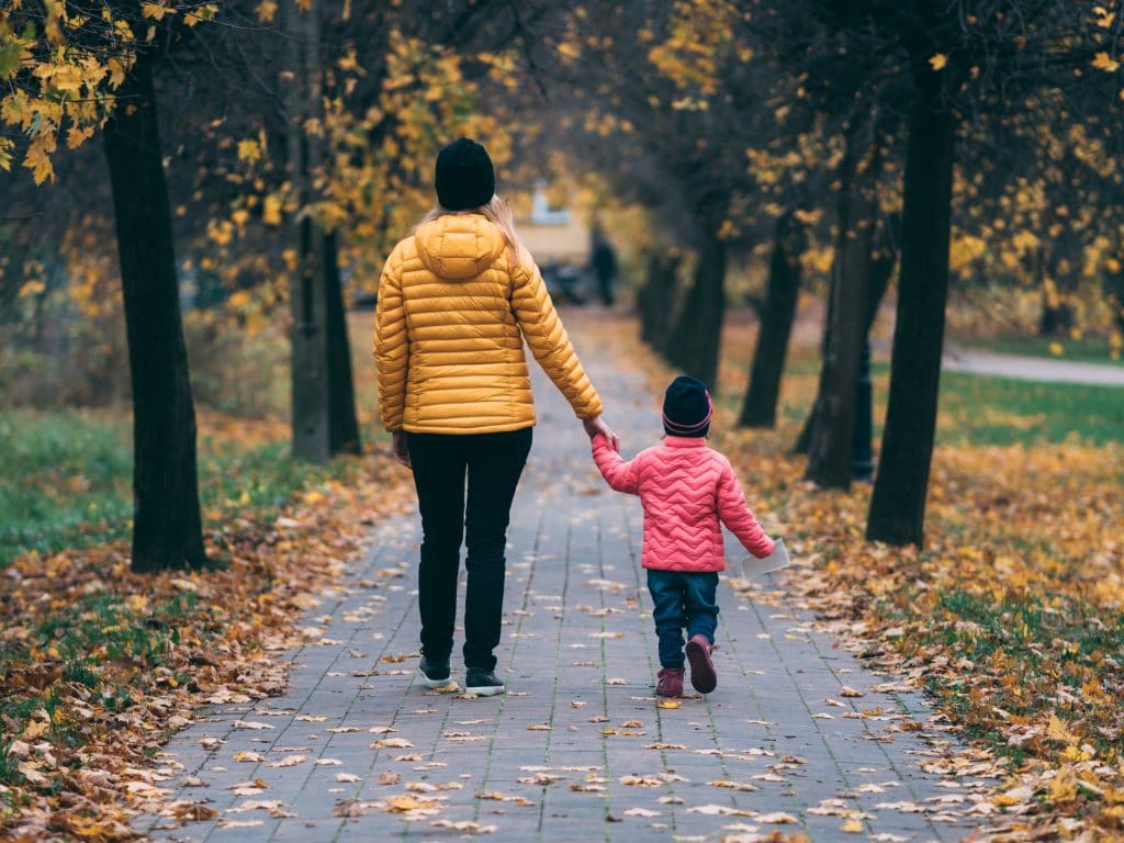 Mãe e filho de mãos dadas caminhando em caminho de parque com folhas de outono caindo