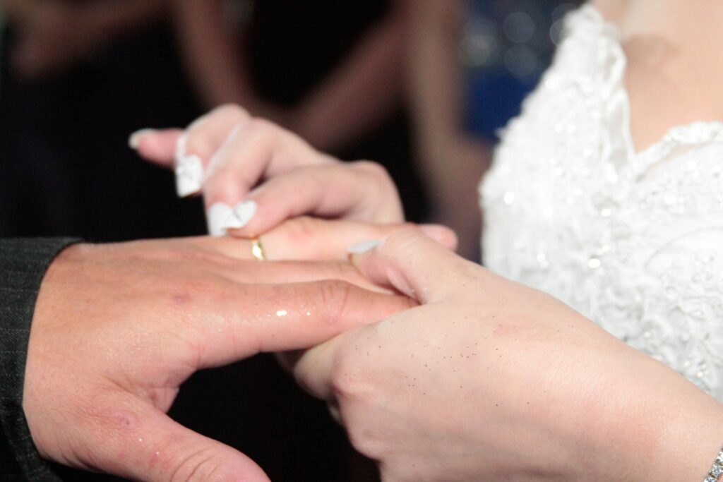 Mulher colocando aliança no dedo da mão esquerda doo seu esposo em uma cerimônia de casamento.