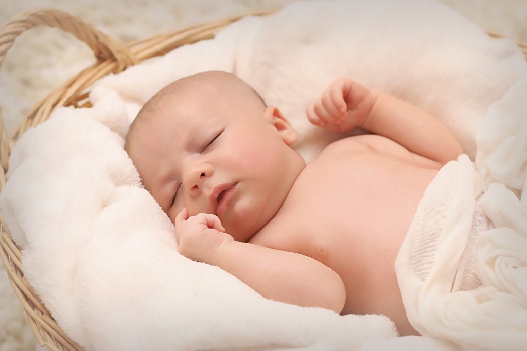 Imagem de um recém nascido dentro de um cesto de vime forrado com um cobertor bem macio na cor brnaca. Ele está dormindo.