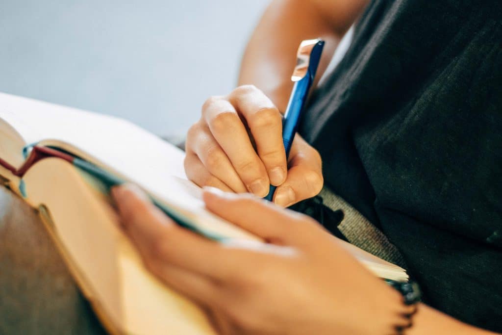 Pessoa escrevendo em um caderno com uma caneta.