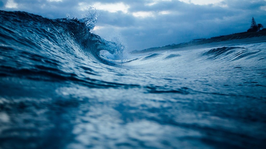 Imagem de um oceano bem azul com uma onda quebrando no começo do mar.