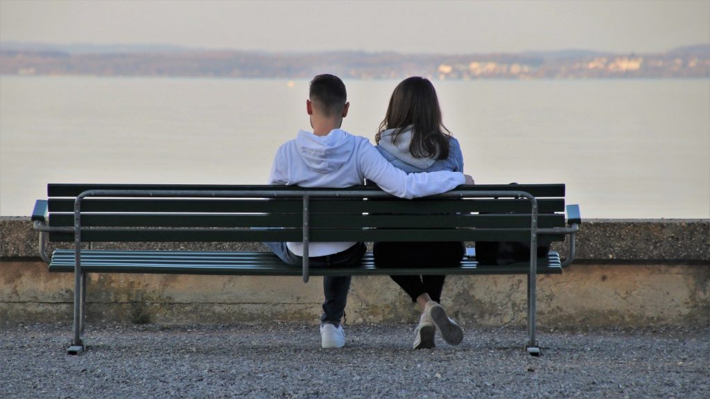 Imagem de um casal de jovens menino e menina sentados em um banco em frente a um lindo lago. Eles estão abraçados e observado a paisagem em silêncio.