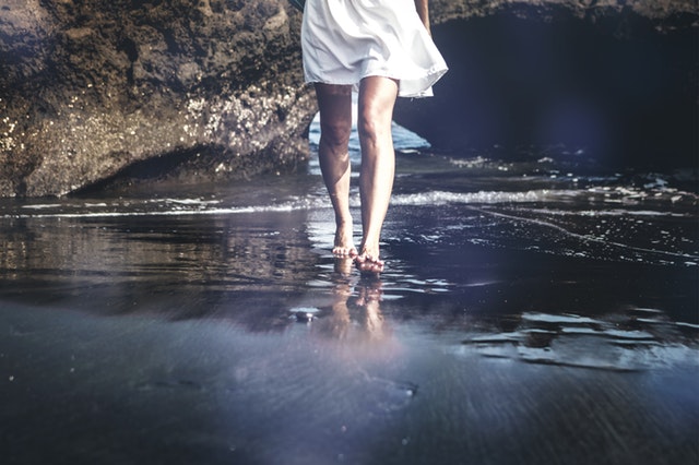 Pernas de mulher caminhando na areia da praia