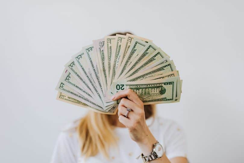 Mulher segurando notas de dinheiro cobrindo seu rosto