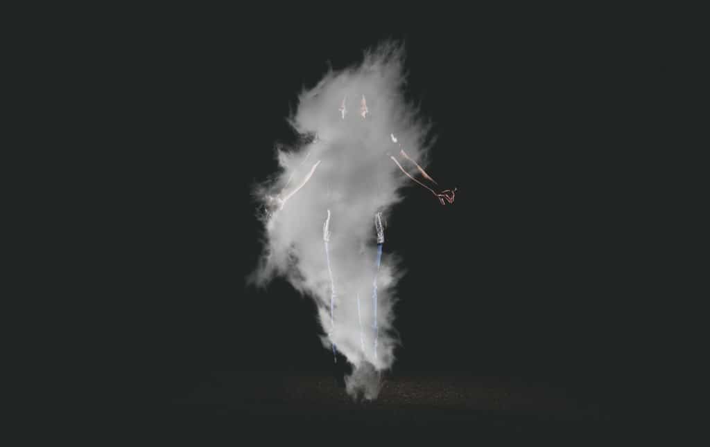 Homem no ar durante um pulo, coberto por fumaça branca, em um fundo preto