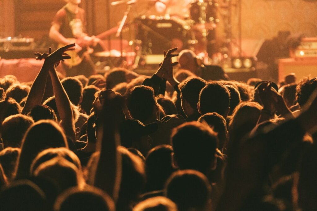 Silhueta de uma multidão de pessoas em um show de rock, com a banda tocando ao fundo.