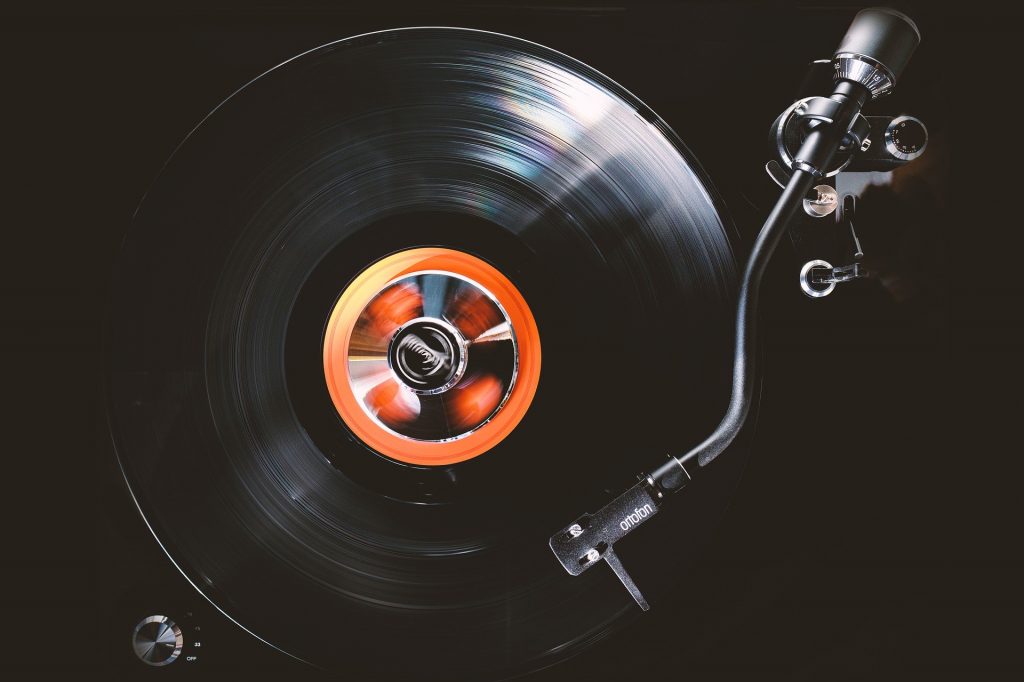 Imagem de um disco de vinil em uma vitrola antiga. Sobre ele,  agulha da vitrola está em destaque.