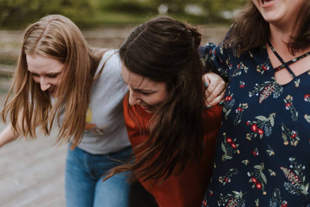 Três mulheres abraçadas e sorrindo na rua