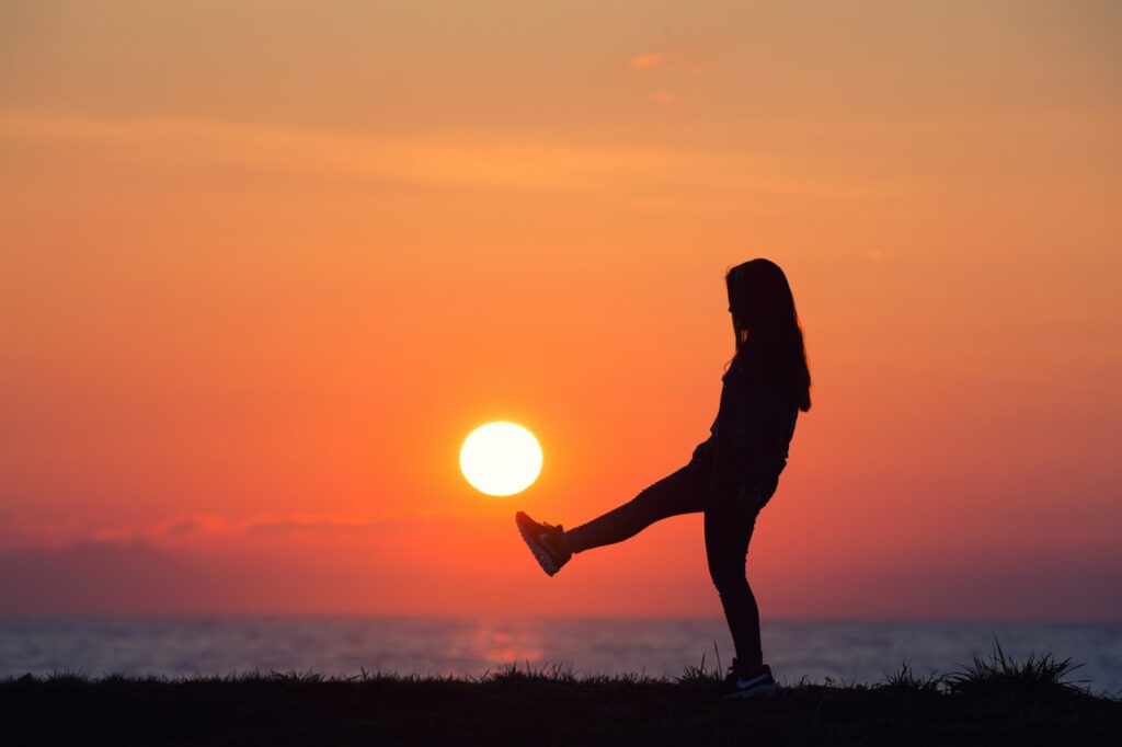 Silhueta de mulher com pôr-do-sol ao fundo como se ela estivesse chutando-o