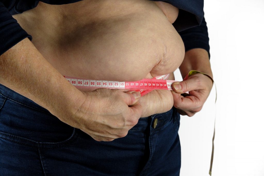 Imagem de um homem com uma barriga bem grande. Ele está medindo a sua barriga com uma vita métrica.
