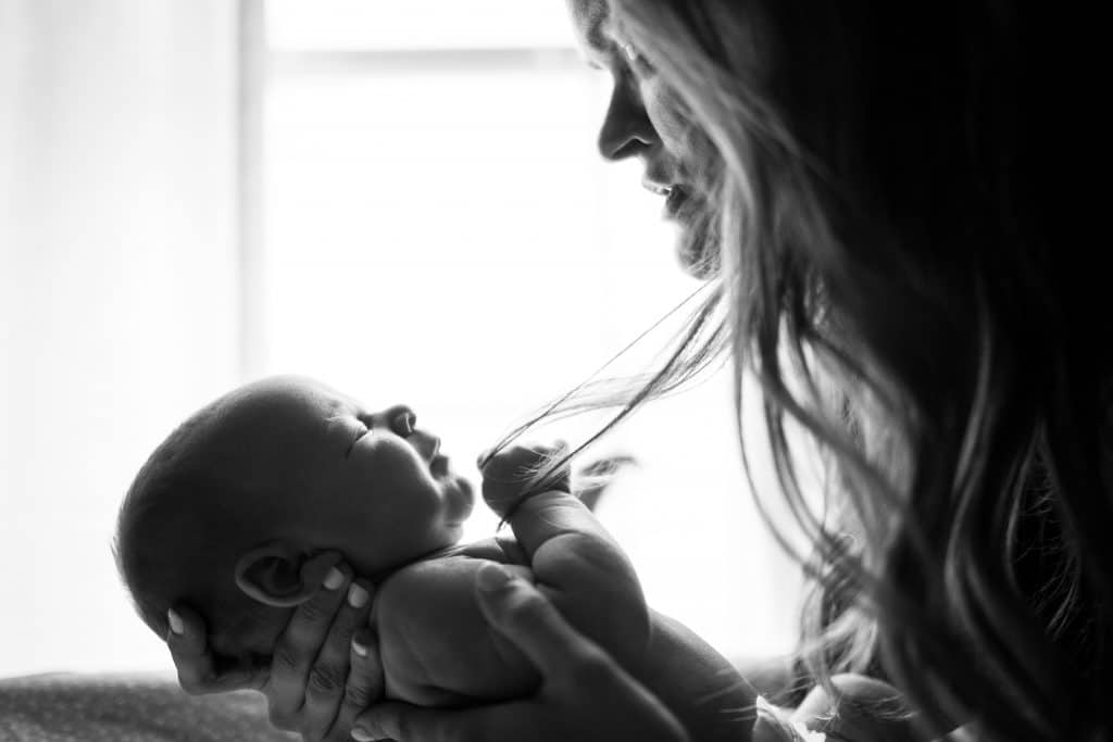 Mãe segurando filho recém-nascido em frete ao corpo em foto preta e branca