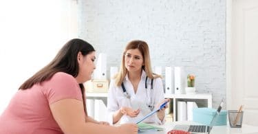 Mulher obesa em consulta com médica, que lhe apresenta informações em uma prancheta.
