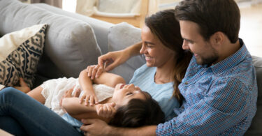 Família deitada no sofá da sala sorrindo