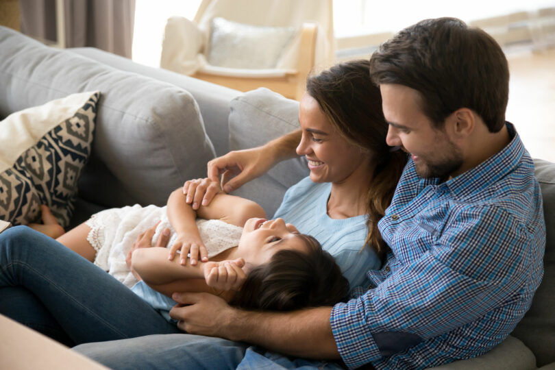 Família deitada no sofá da sala sorrindo