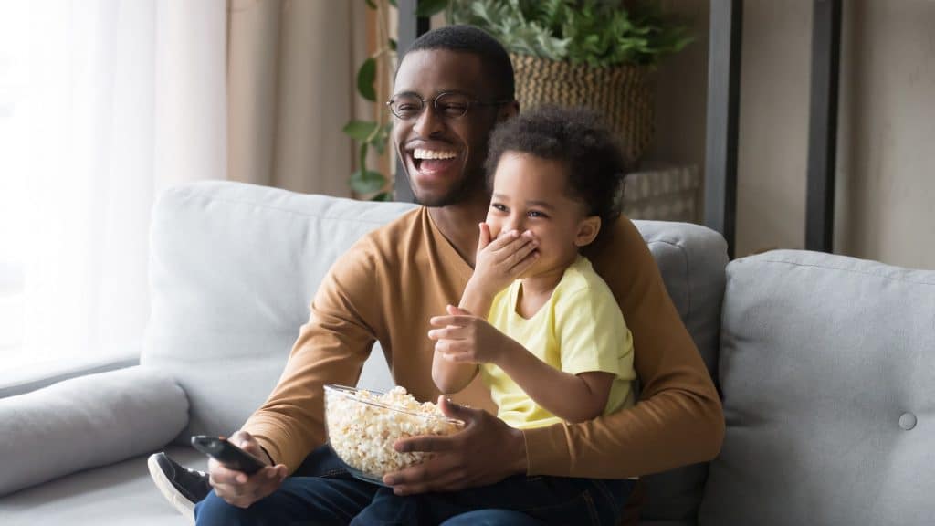 Pai e filho assistindo televisão segurando pipoca