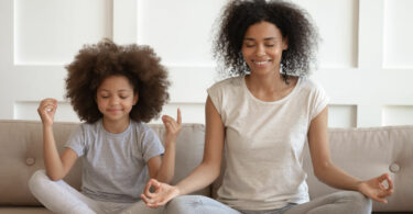 Mãe e filha meditando em sofá