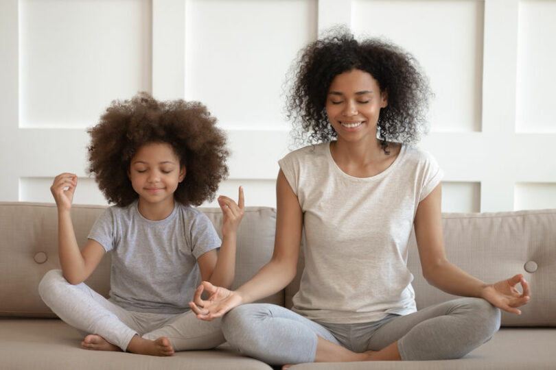 Mãe e filha meditando em sofá