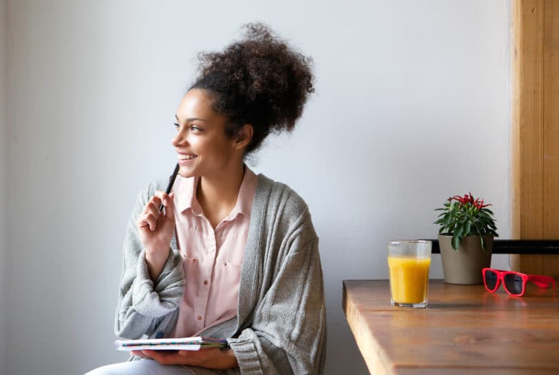 Mulher pensativa sorrindo segurando um caderno