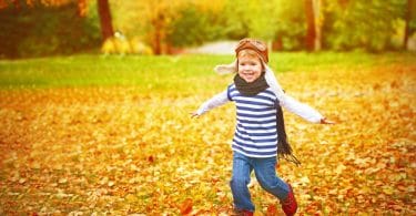Criança feliz correndo em folhas de outono