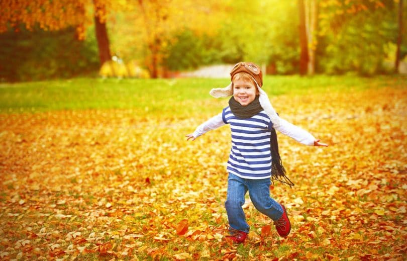 Criança feliz correndo em folhas de outono