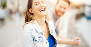 Mulher sorrindo na rua com um homem ao seu lado.