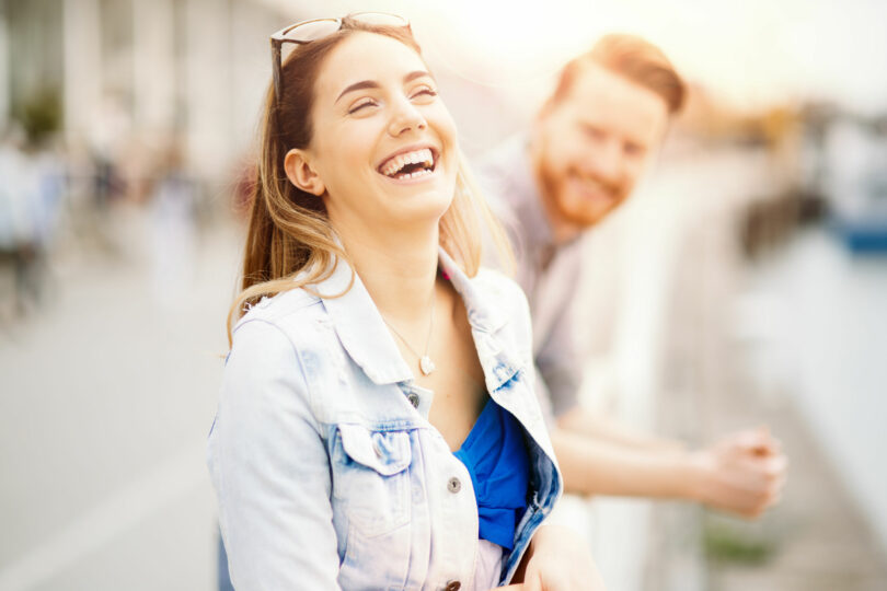 Mulher sorrindo na rua com um homem ao seu lado.