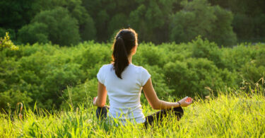 Mulher meditando em gramado no alto de montanha