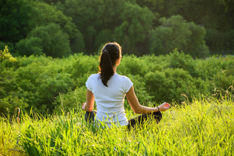 Mulher meditando em gramado no alto de montanha