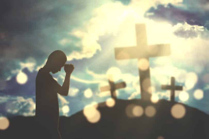 Um homem adora a Deus com três cruzes e luz do sol no céu.