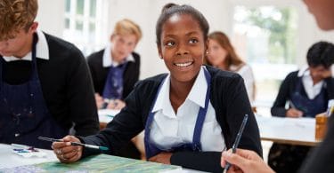 Menina adolescente sorrindo em aula de pintura na escola.