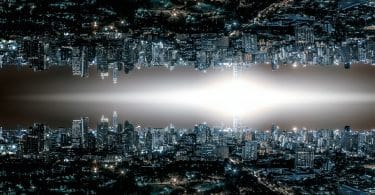 Horizonte de uma cidade grande com muitas luzes acesas em prédios e nas ruas. No centro da imagem existe uma luz em formato de losango. Na parte superior, a mesma imagem da parte de baixo mas de ponta-cabeça, como um reflexo.