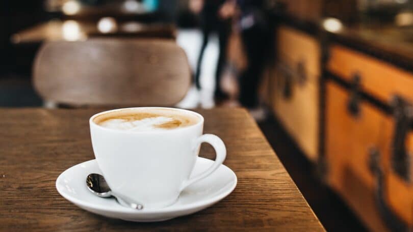 Imagem de uma xícara de capucciono em cima de uma mesa de restaurante