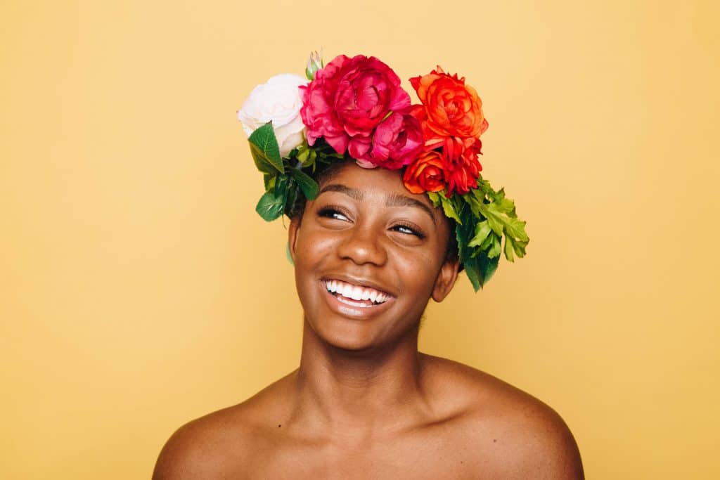 Mulher sorridente com uma coroa de flores sobre a cabeça, olhando para o lado.