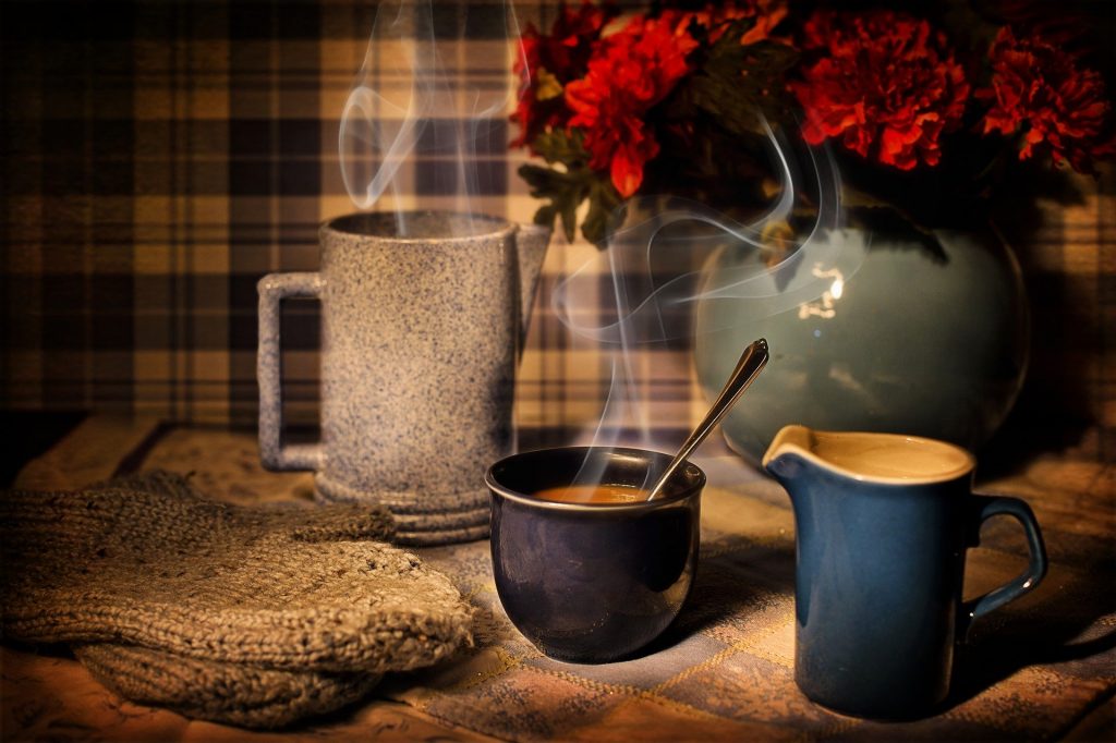 Imagem de uma mesa decorada com juta. Sobre ela uma caneca de café, um bule e um arranjo de flores vermelhas decoram o espaço.
