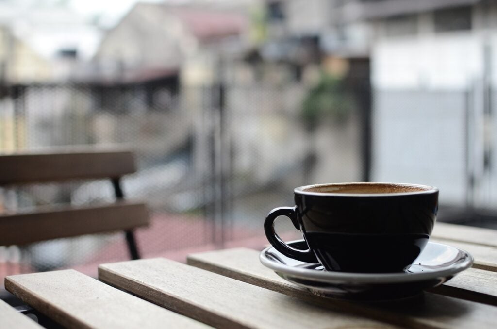 Imagem de uma xícara de café de porcelana na cor marrom. A xícara está disposta sobre uma mesa de madeira.