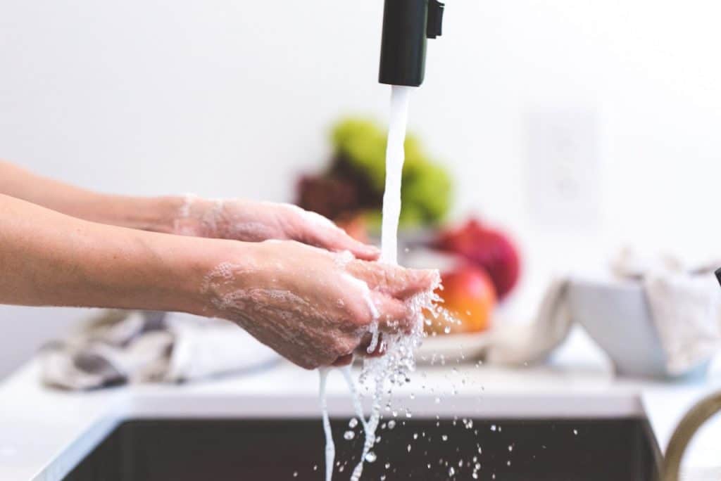 Mãos ensaboadas de uma pessoa lavando louças na pia de uma cozinha.