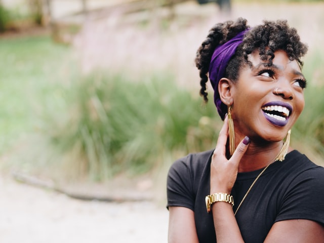 Mulher negra sorrindo com sua mão no pescoço.