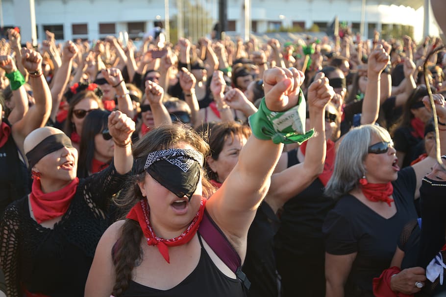 Grupo de mulheres gritando em protesto com os punhos para o alto.