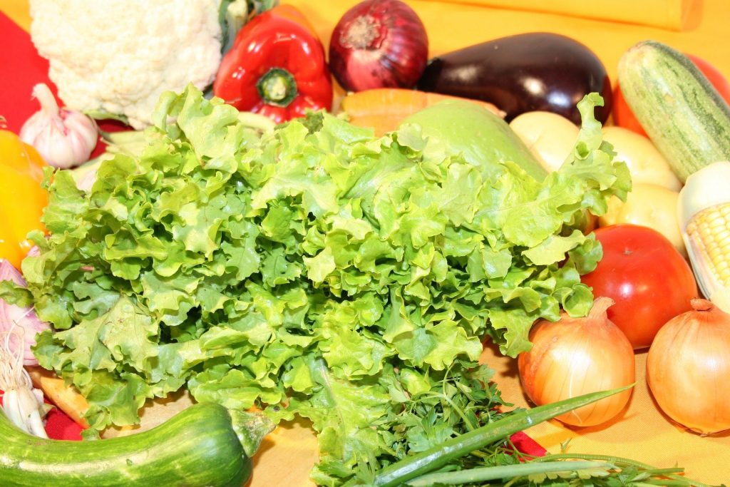 Imagem de uma bancada cheia de alimentos saudáveis como: verduras e legumes como: abobrinhas, cheiro verde, alho, couve flor, pimentão, cebola, tomate, batata, milho e cenoura.