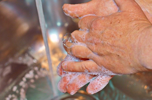 Mãos unidas com sabão enxaguando com torneira ao fundo