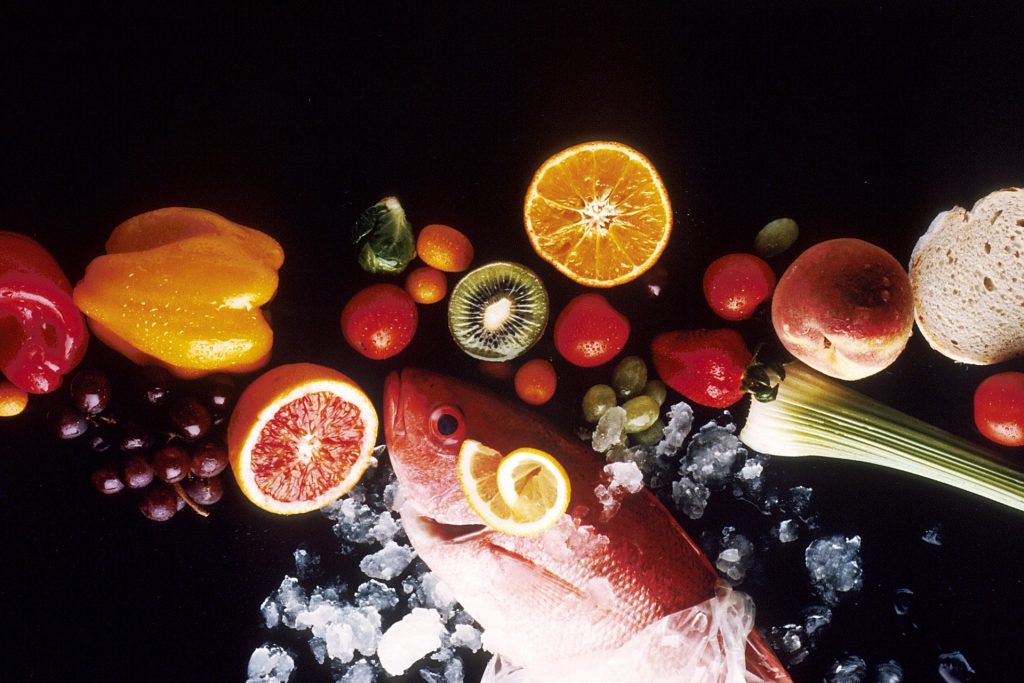 Imagem composta por vários alimentos saudáveis como: salmão, uvas, laranja, kiwi, limão, pêssego alho poró.