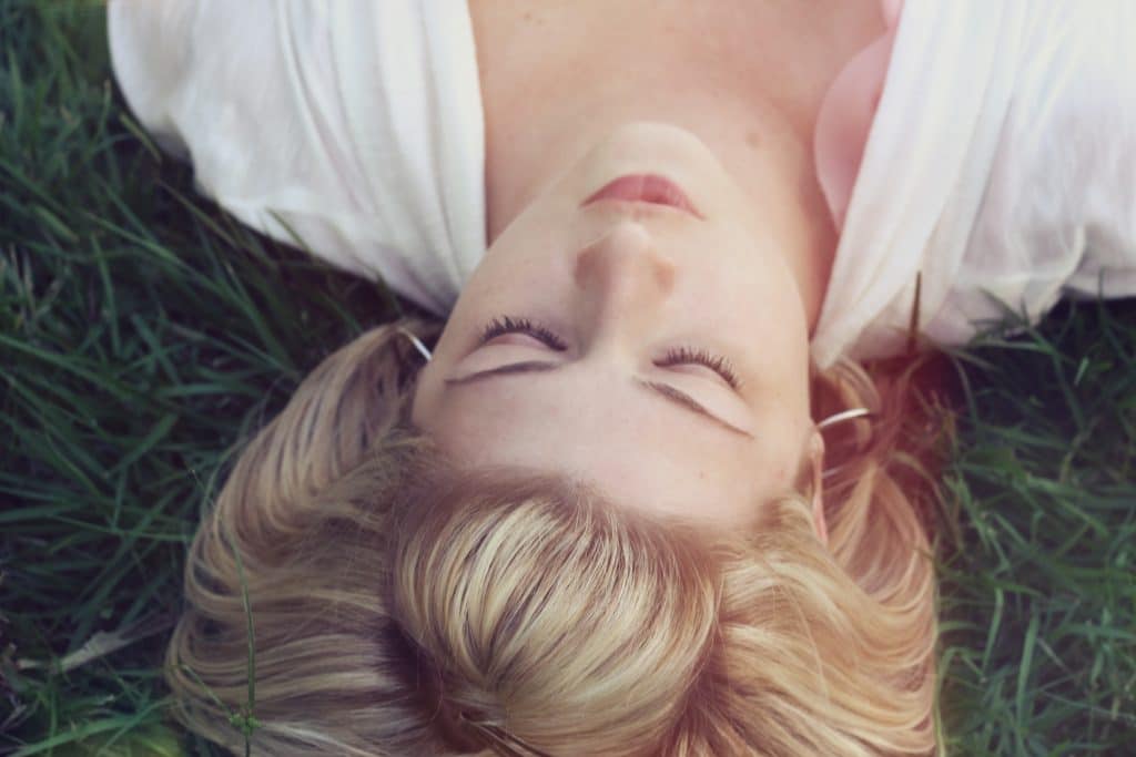 Mulher deitada no gramado com os olhos fechados